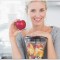 Blonde woman leaning on her juicer full of fruit and holding red apple at home in kitchen